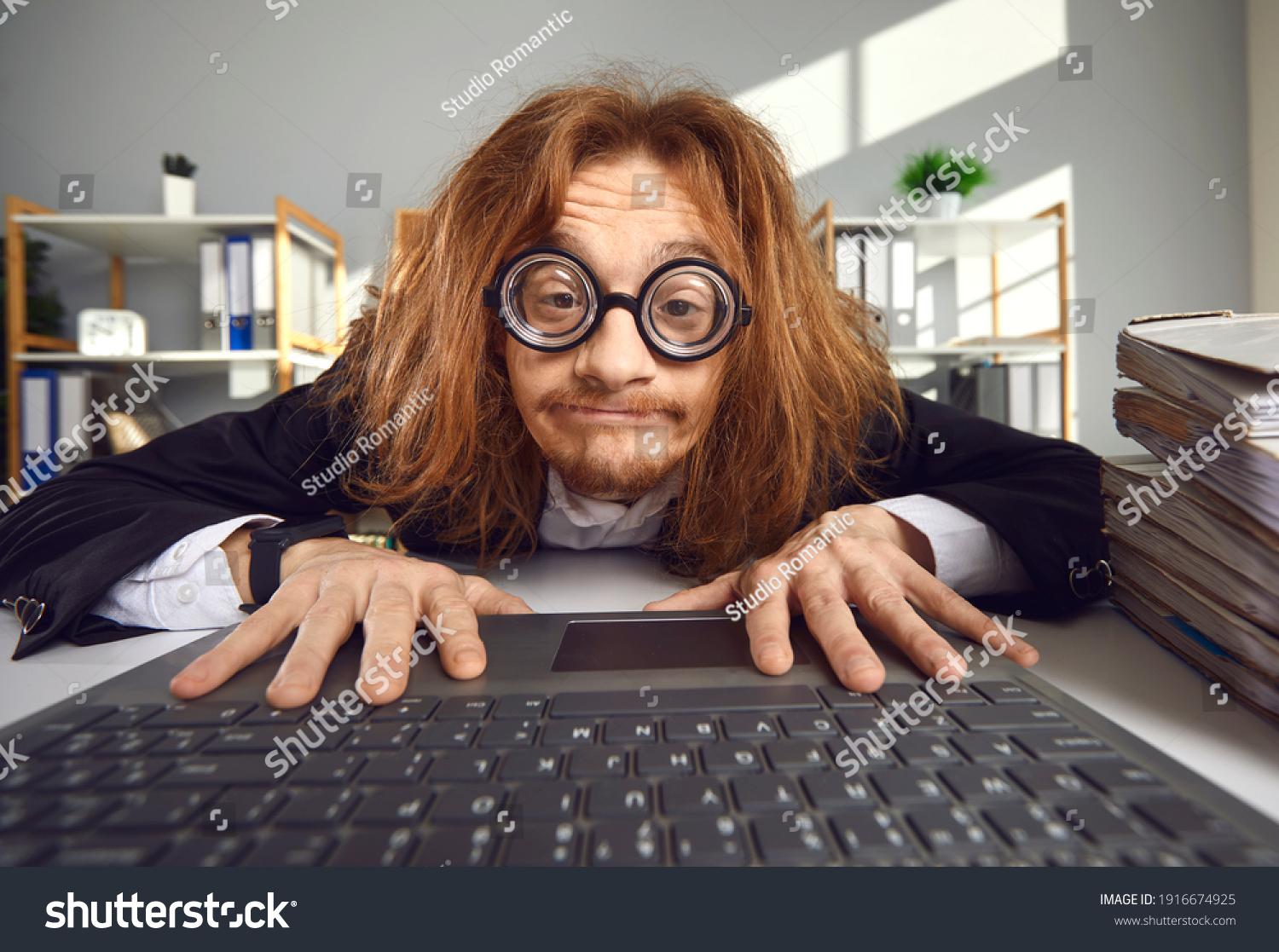 Funny nerd in round thick lens glasses sitting at desk and using laptop. Crazy looking office worker or computer geek typing on keyboard, searching for information on the Internet or doing accounts #1916674925