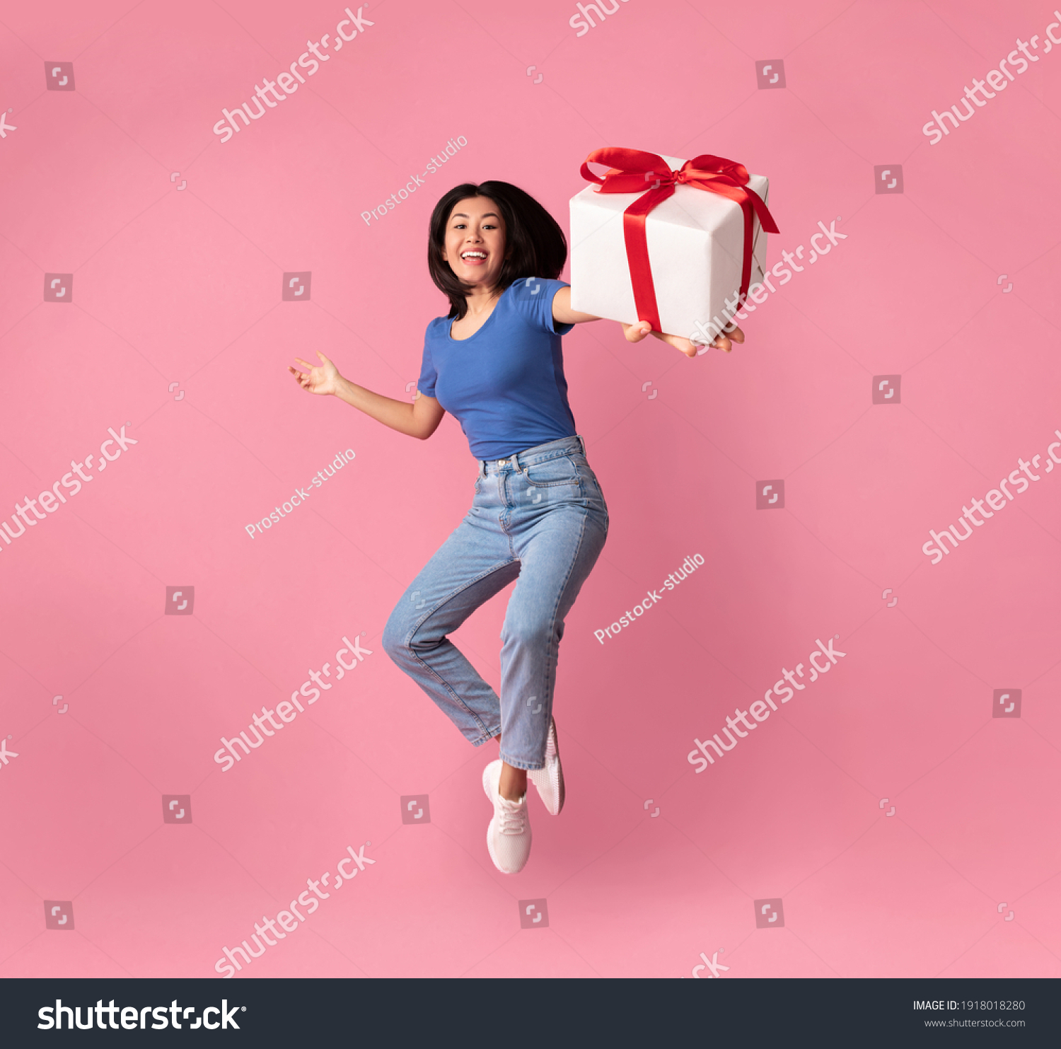 Full length vertical photo of jumping high excited asian lady holding and showing present box close to camera, giving gift isolated over pastel pink studio background. Greeting And Celebration #1918018280