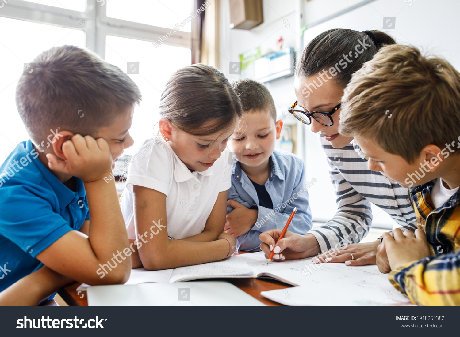 Female teacher helps school kids to finish they lesson.They sitting all together at one desk.	
 #1918252382