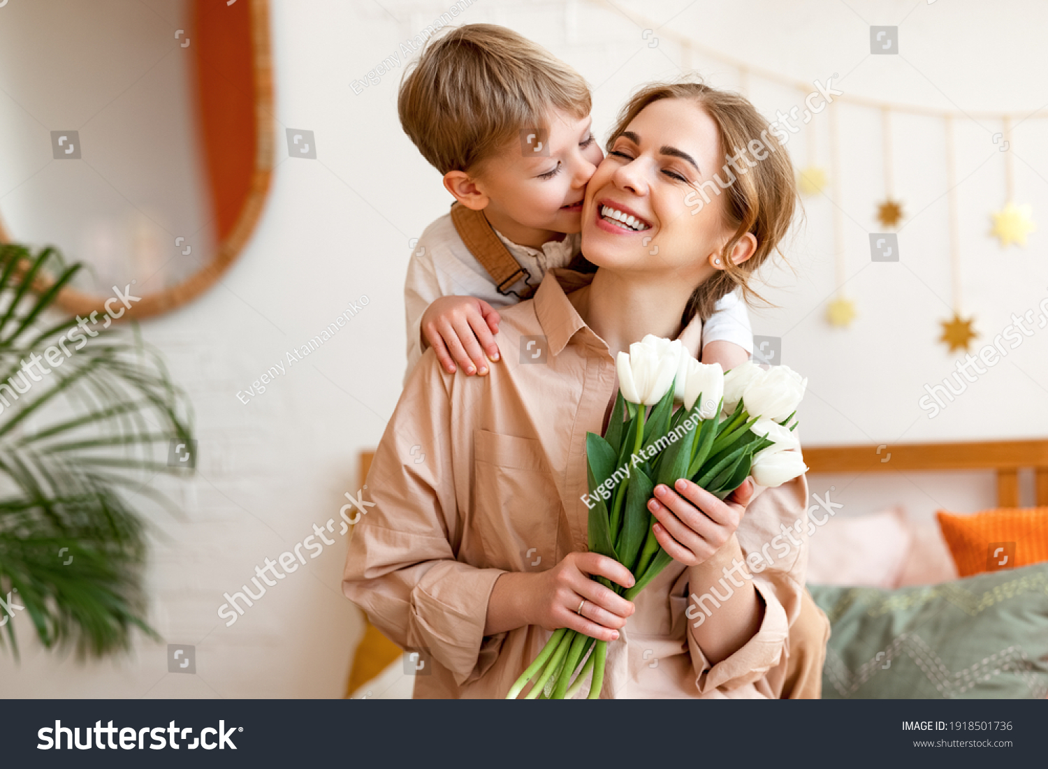 tender son kisses the happy mother and gives her a bouquet of tulips, congratulating her on mother's day during holiday celebration at home #1918501736
