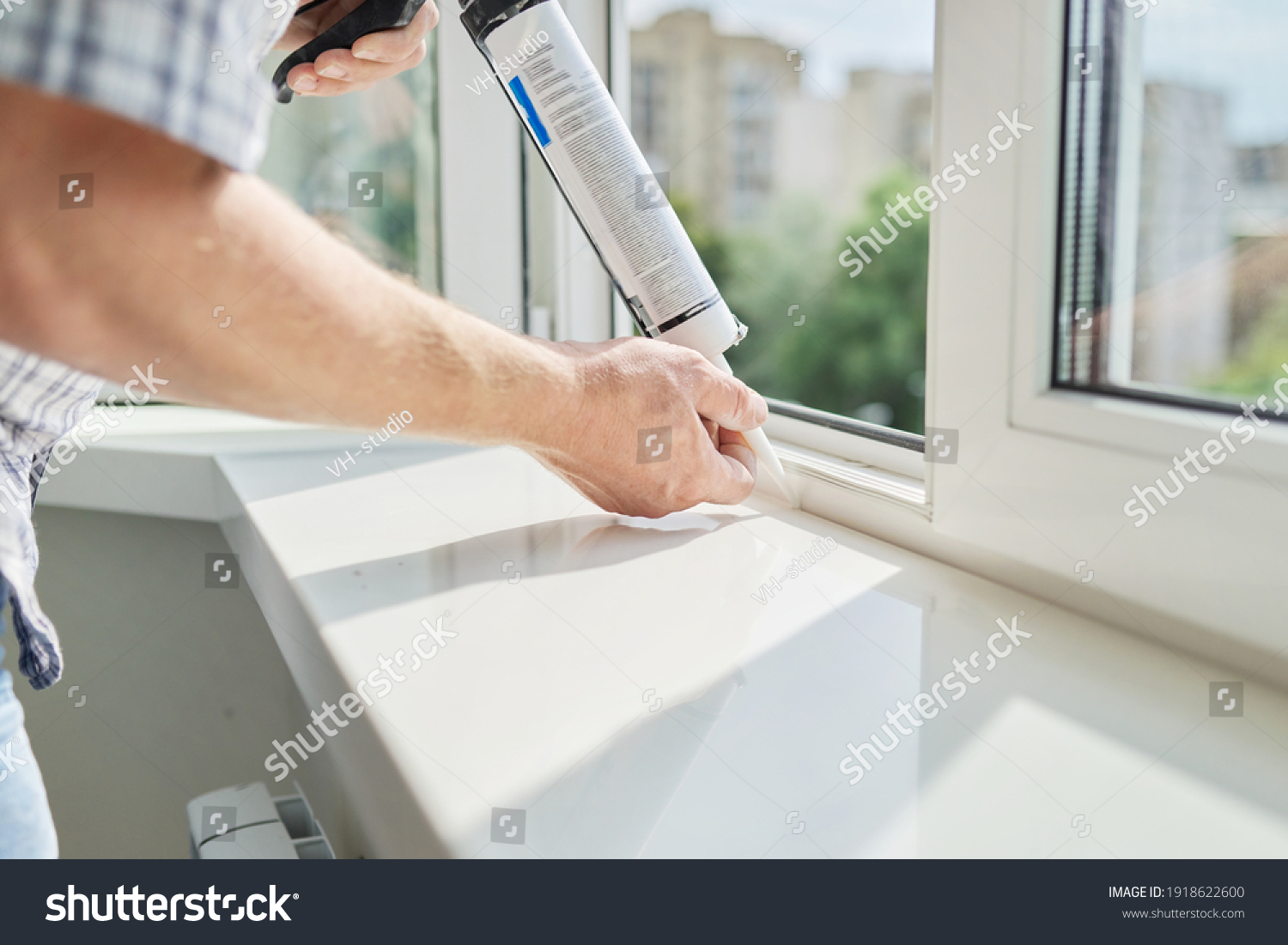 Artificial stone window sill, installation, technological process. Repair, construction of house, apartment. Worker with construction syringe fills seam between sill and window with silicone sealant #1918622600