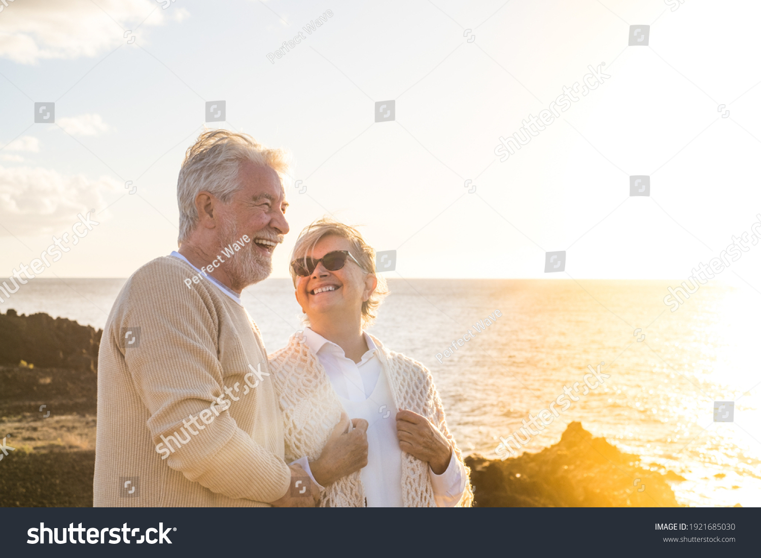 close up and portrait of two happy and active seniors or pensioners having fun and enjoying looking at the sunset smiling with the sea - old people outdoors enjoying vacations together #1921685030