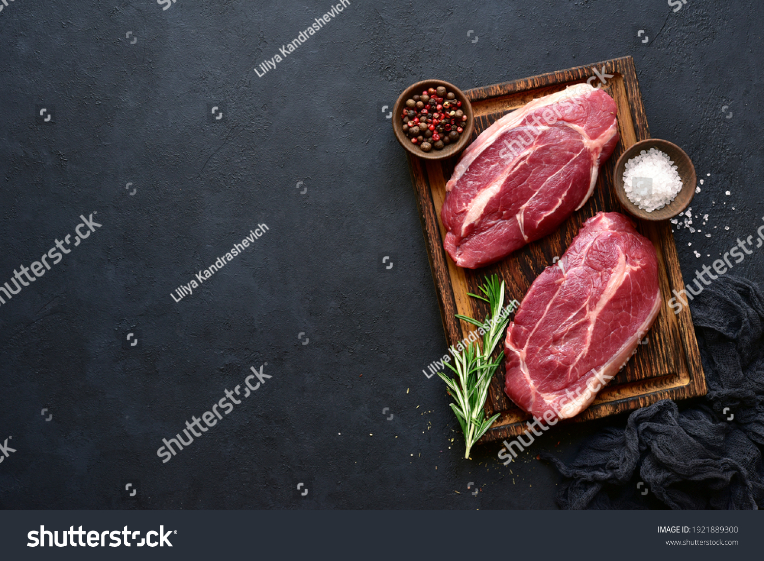 Raw organic marbled beef steaks with spices  on a wooden cutting board on a  black slate, stone or concrete background. Top view with copy space. #1921889300