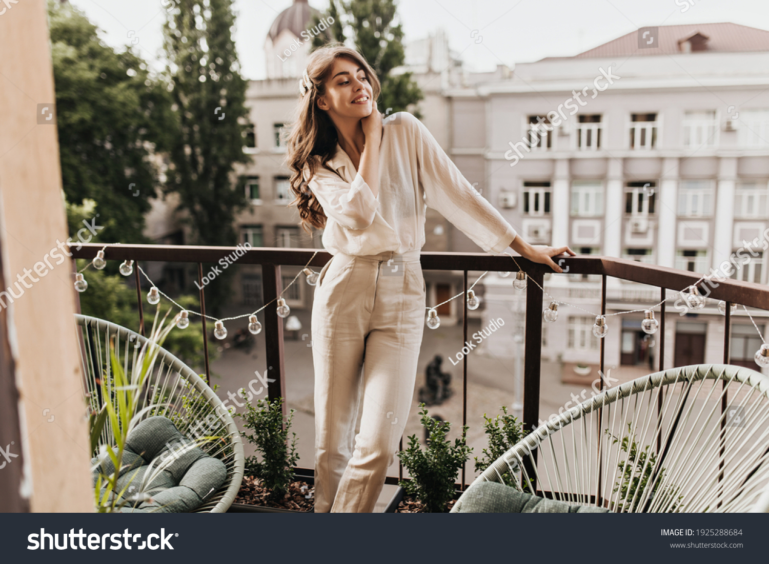 Cool woman in beige outfit smiling on terrace. Happy young lady in stylish pants and shirt poses on balcony and enjoys sunny weather #1925288684