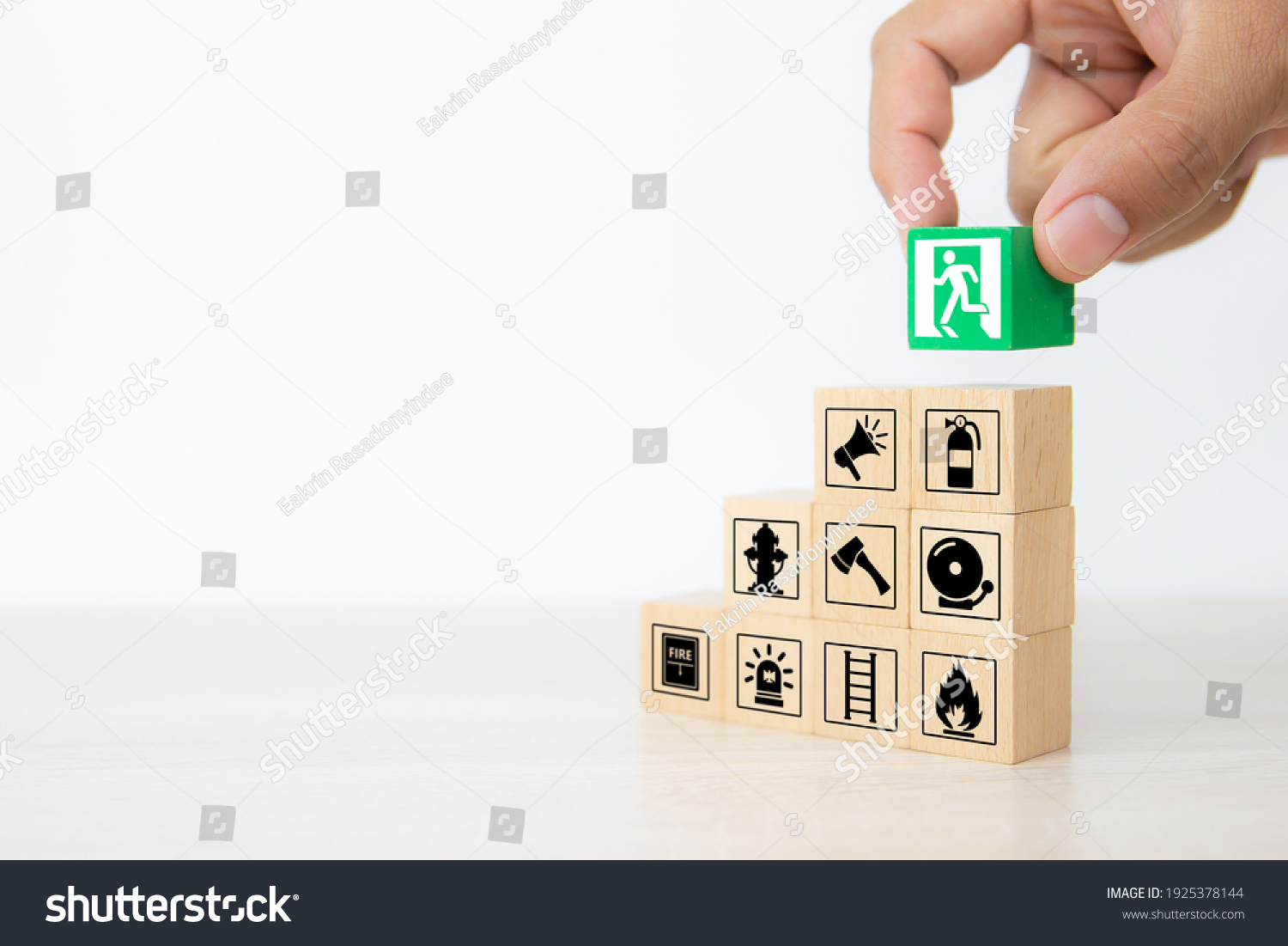 Close-up hand choose wooden toy blocks stacked with door exit sing icon with fire extinguisher and fire protection symbol for safety prevent and protect accident of emergency and rescue. #1925378144
