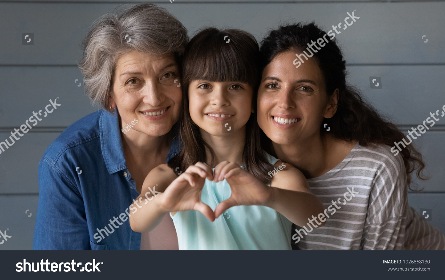 Close up family portrait of happy three generations of Hispanic women pose together show love heart hand gesture. Smiling little Latino girl child with young mother and senior grandmother feel united. #1926868130