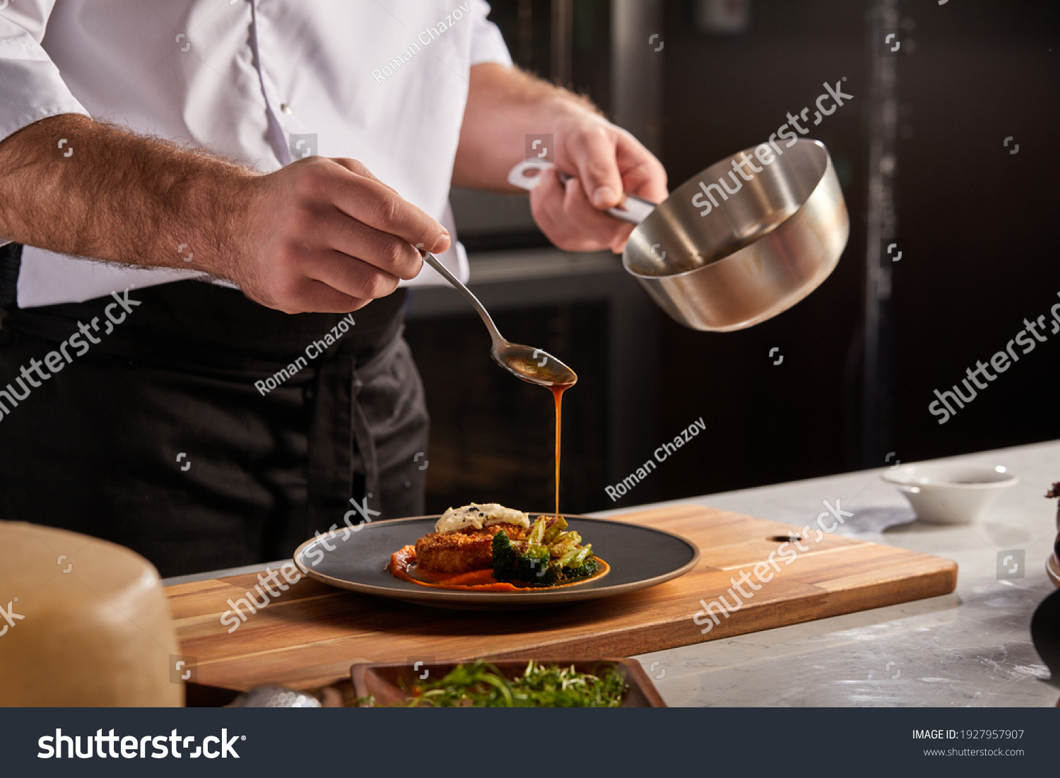 Cook in apron adding some sauce to dish. Cropped chef preparing food, meal, in kitchen, chef cooking, Chef decorating dish, closeup #1927957907