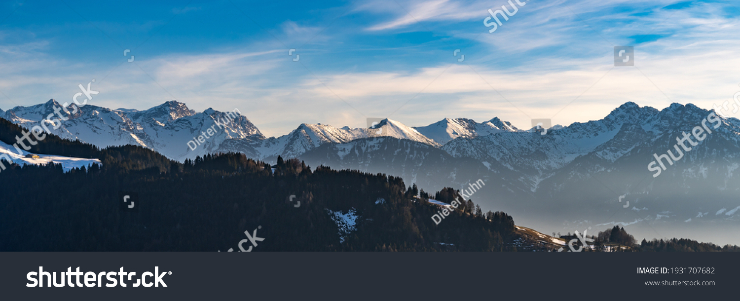 Panorama view of the snowy mountains between Switzerland, Liechtenstein and Austria. in foreground Austrian Alp with meadows and huts in the middle of the woods and in Background mountain range peaks #1931707682