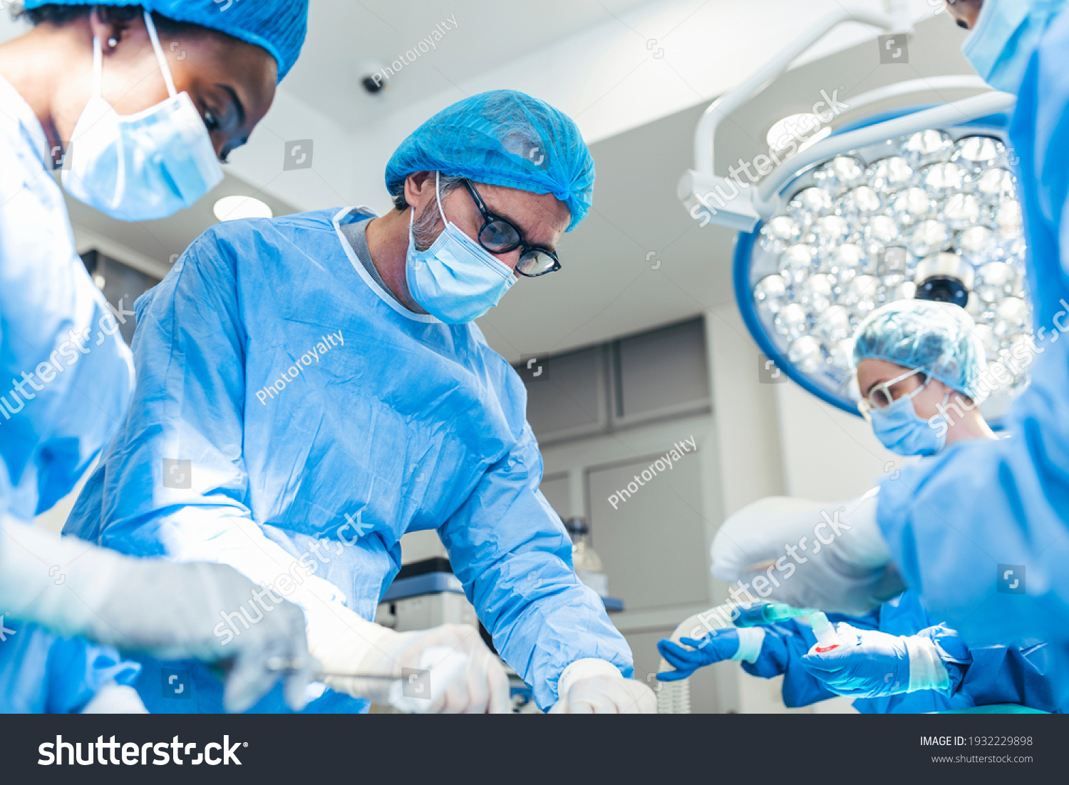 Surgery operation. Group of surgeons in operating room with surgery equipment. Medical background, selective focus. Surgeon team working together while operation #1932229898