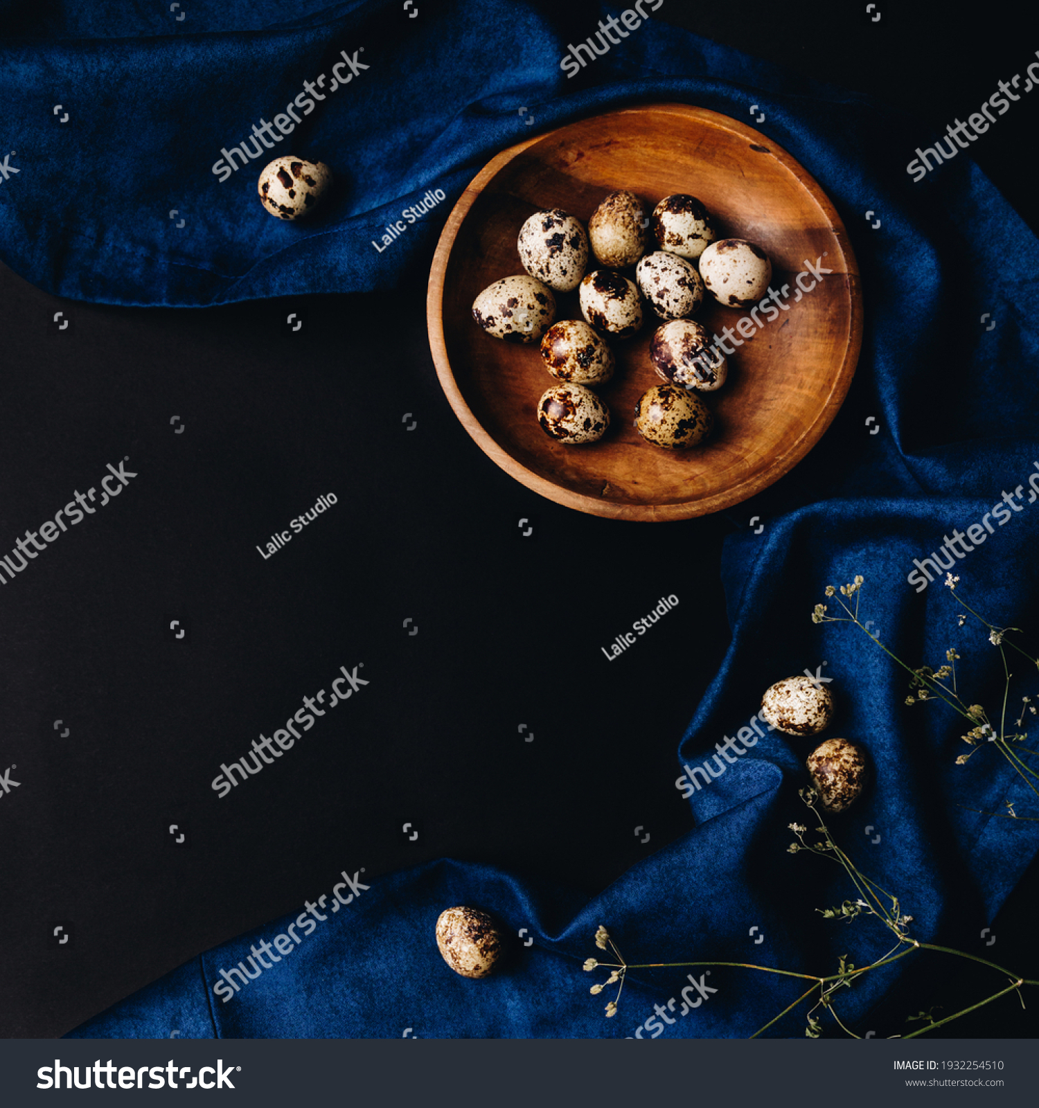 Easter table settings, minimal concept of fresh quail eggs in the wooden bowl on the dark background with blue saten or silk around and dry flowers in the corner. Spring healthy idea. #1932254510