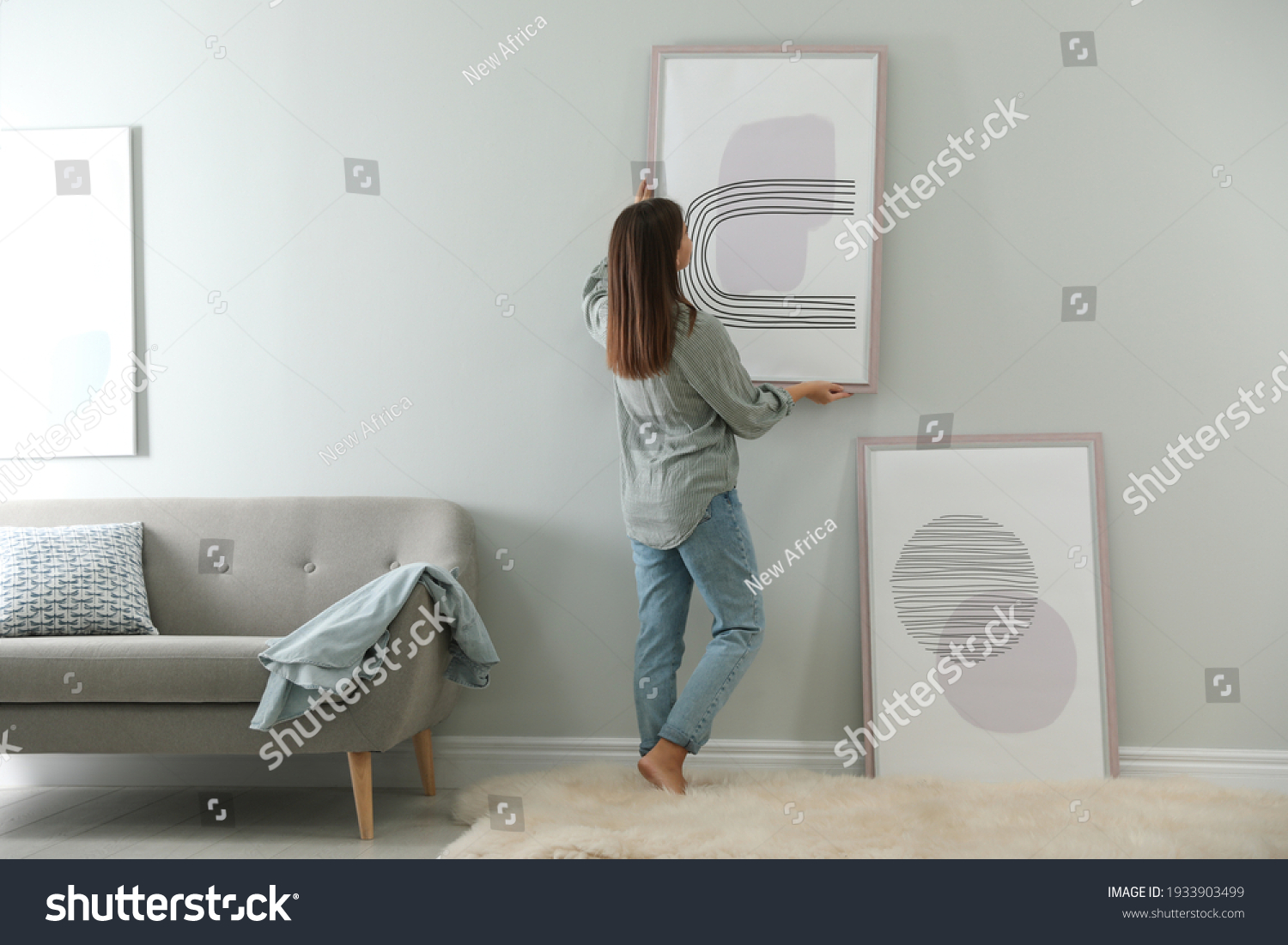 Woman hanging picture on wall in room. Interior design #1933903499
