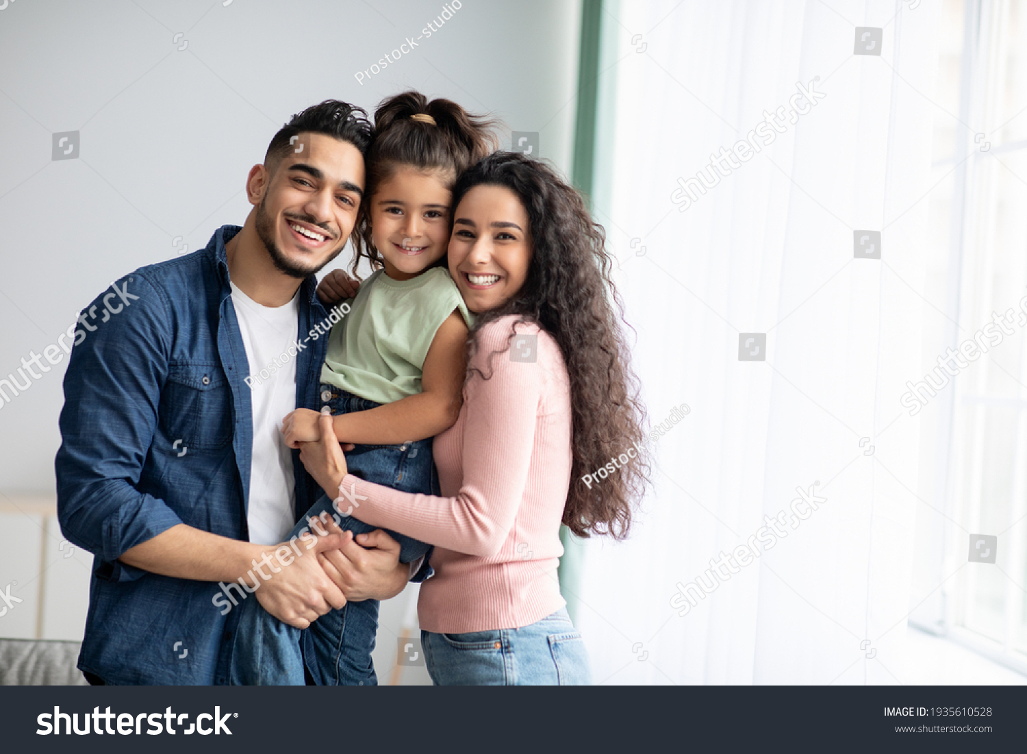 Portraif Of Happy Arabic Parents Posing With Their Little Daughter At Home #1935610528