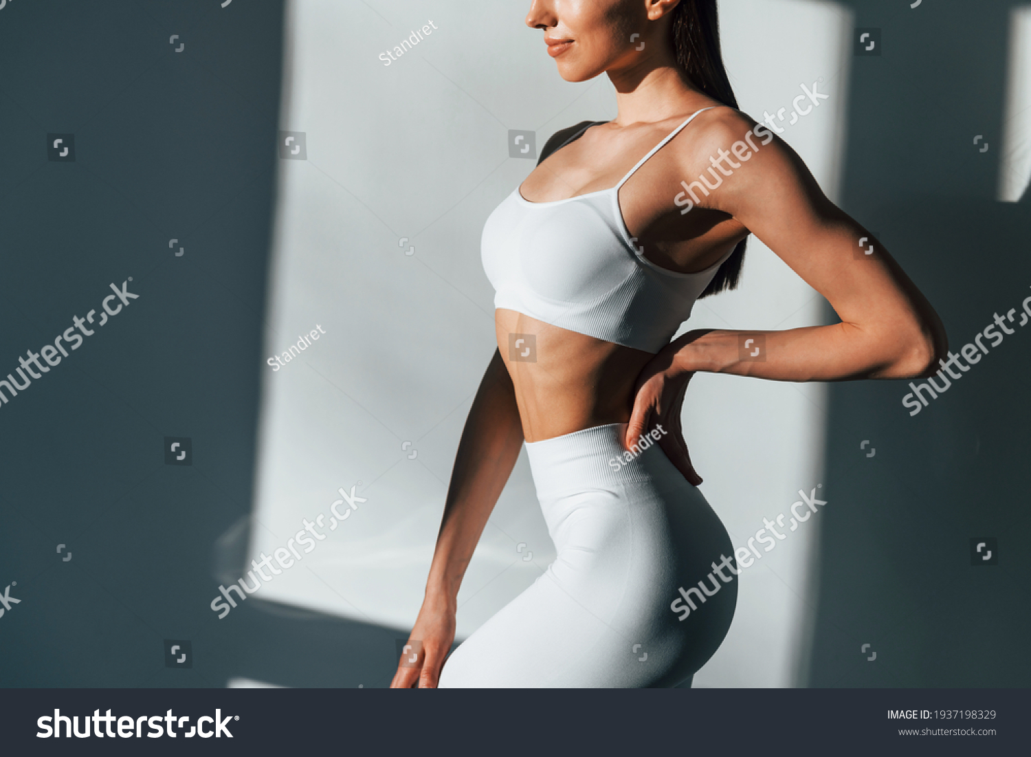 In white sportive clothes. Young caucasian woman with slim body shape is indoors at daytime. #1937198329