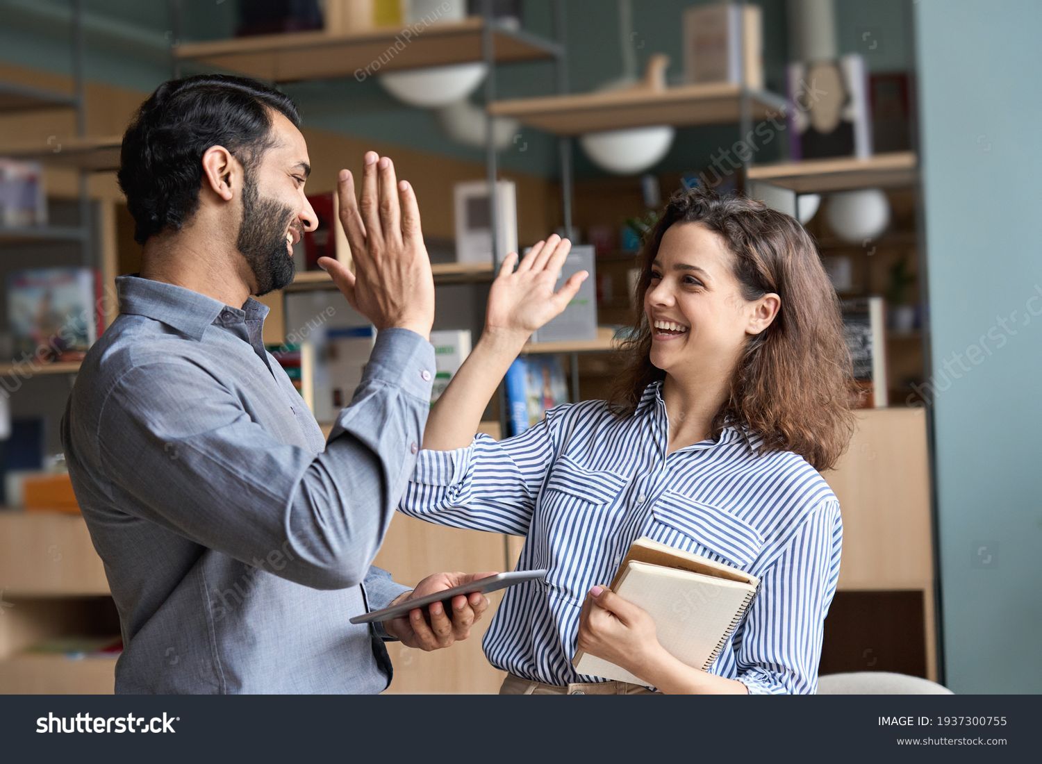 Two happy friendly diverse professionals, teacher and student giving high five standing in office celebrating success, good cooperation result, partnership teamwork and team motivation in office work. #1937300755