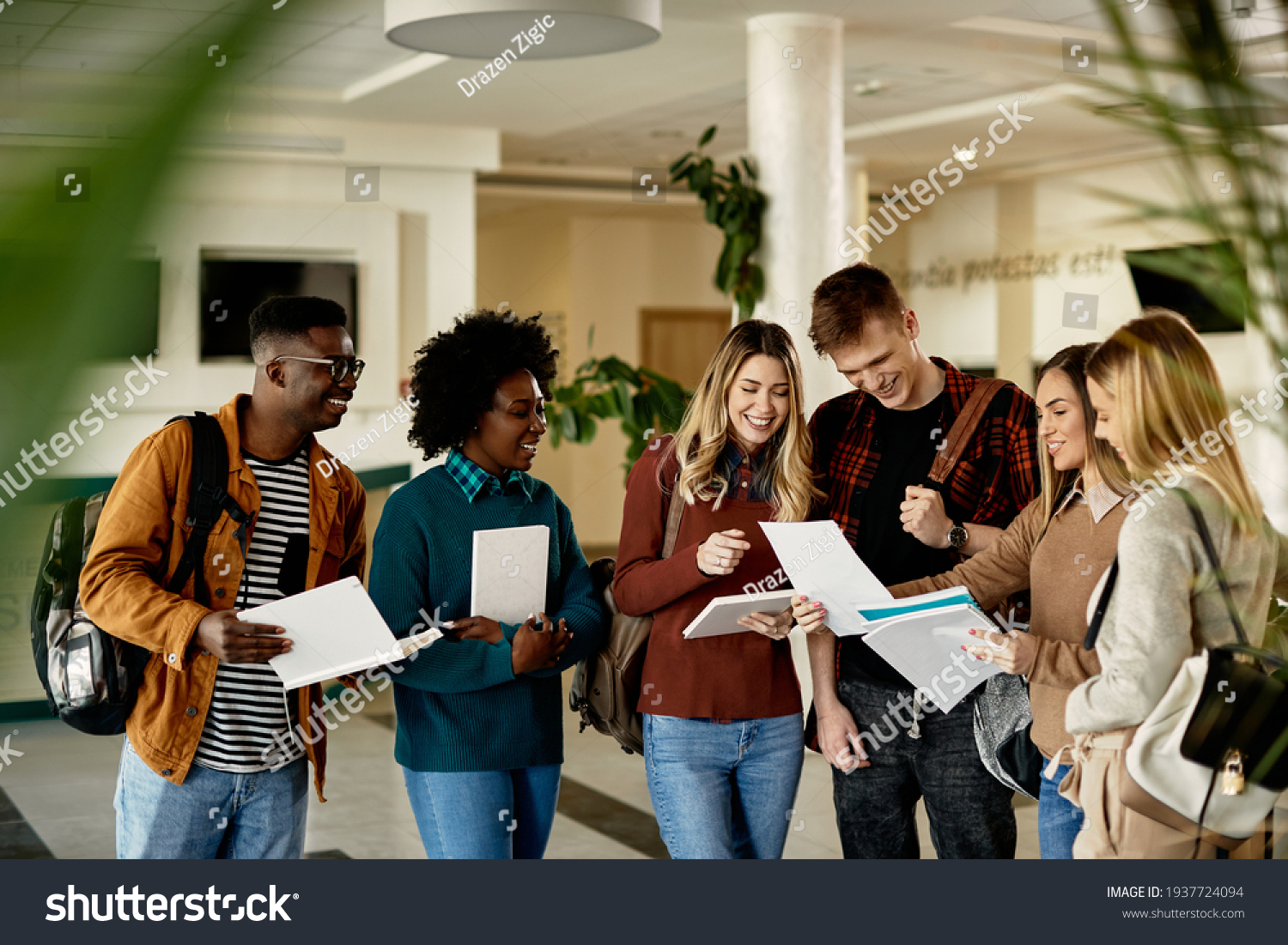 Happy female student showing test results to her friends while standing in a lobby.  #1937724094