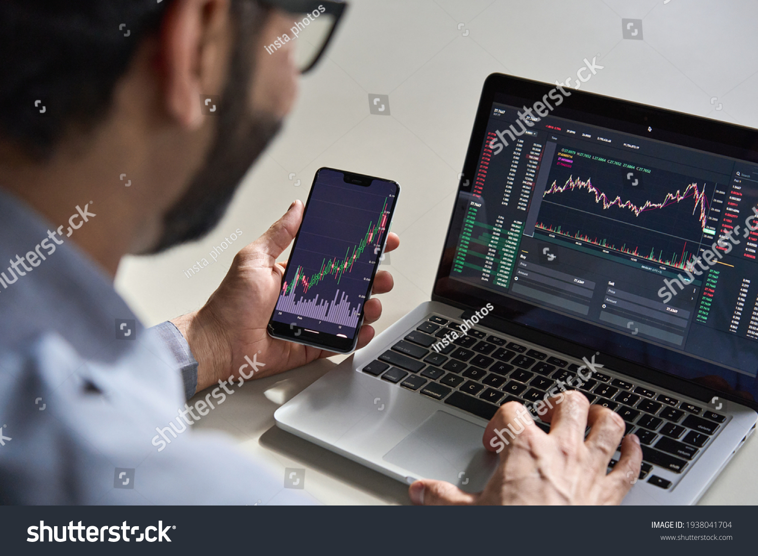 Business man trader investor analyst using mobile phone app analytics for cryptocurrency financial market analysis, trading data index chart graph on smartphone and laptop screen. Over shoulder view #1938041704
