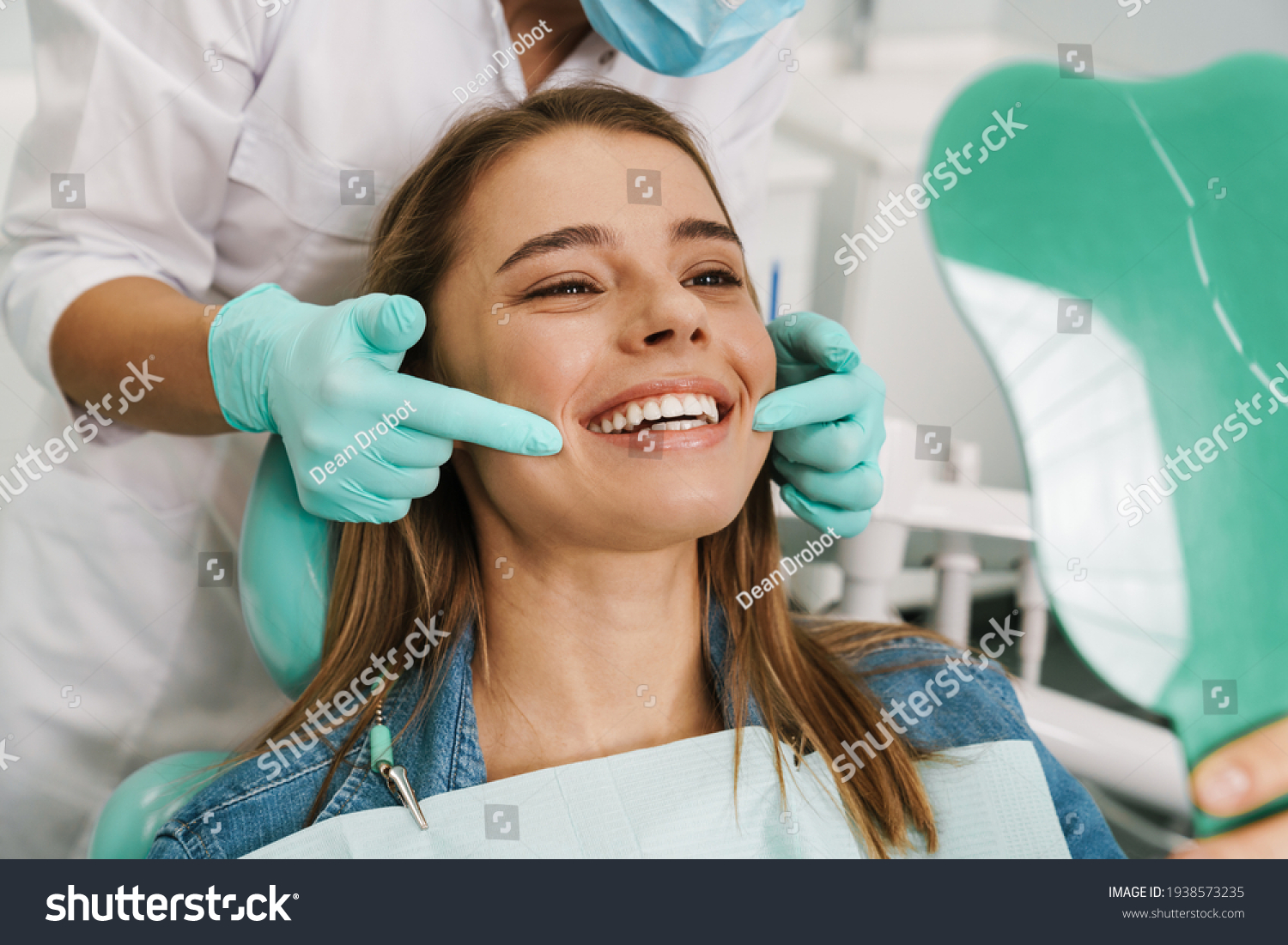 European young woman smiling while looking at mirror in dental clinic #1938573235