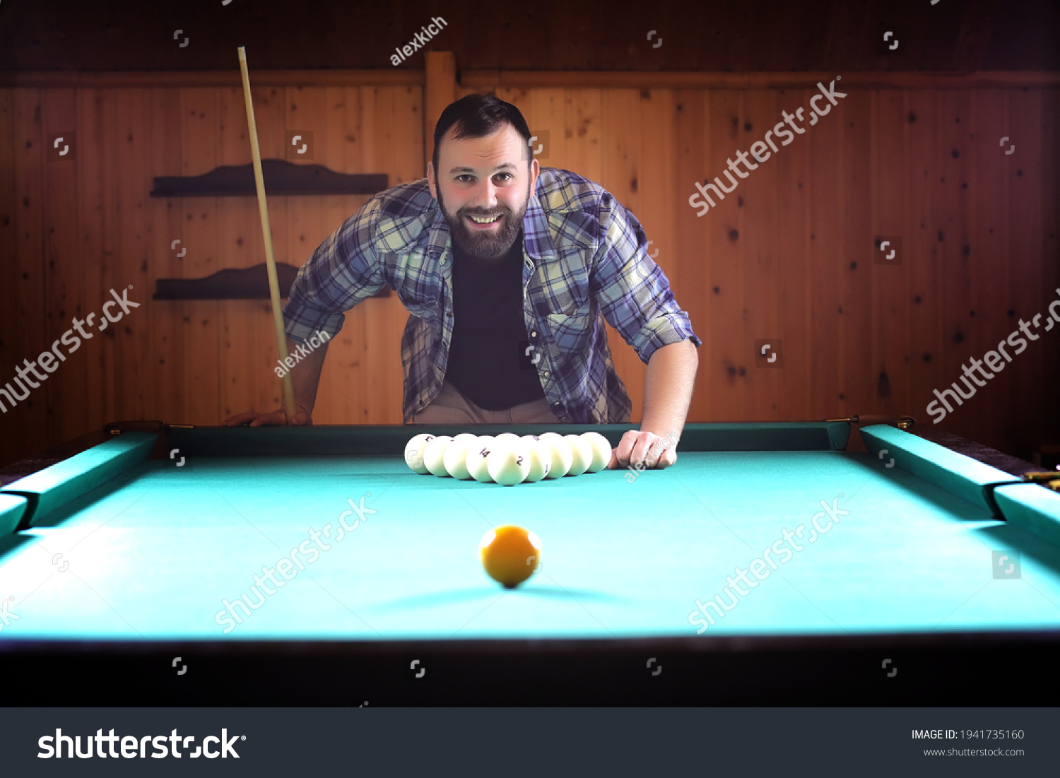 A man with a beard plays a big billiard. Party in 12-foot pool. Billiards in the club game for men. A man with a cue breaks the pyramid. #1941735160