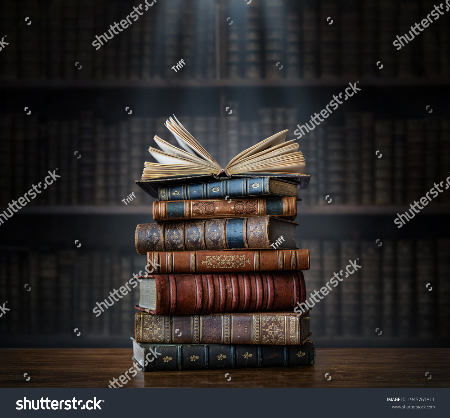 A stack of old books on table against background of bookshelf in library. Ancient books as a symbol of knowledge, history, memory and information. Conceptual background on education, literature topics #1945761811