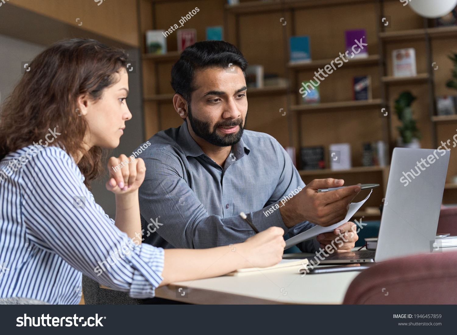 Professional indian teacher, executive or mentor helping latin student, new employee, teaching intern, explaining online job using laptop computer, talking, having teamwork discussion in office. #1946457859