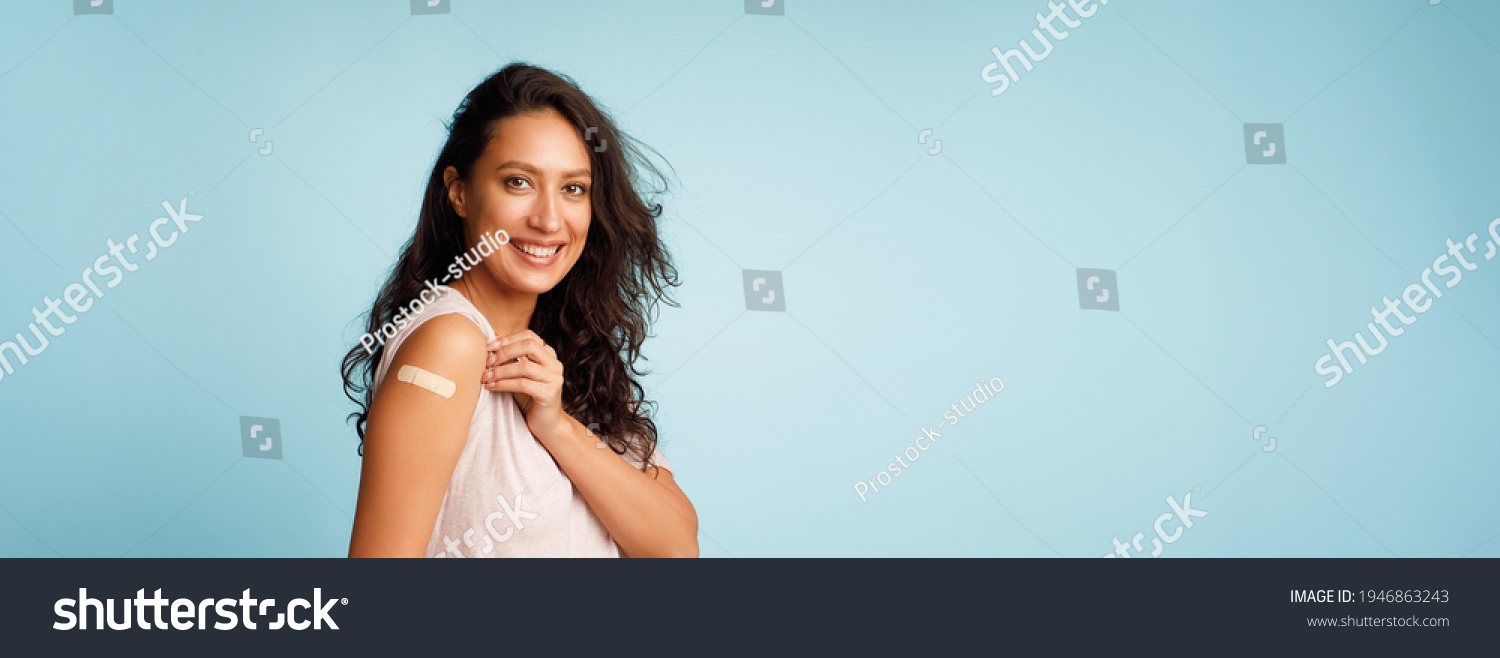 Coronavirus Vaccination Advertisement. Happy Vaccinated Woman Showing Arm With Plaster Bandage After Covid-19 Vaccine Injection Posing Over Blue Background, Smiling To Camera. Panorama, Blank Space #1946863243