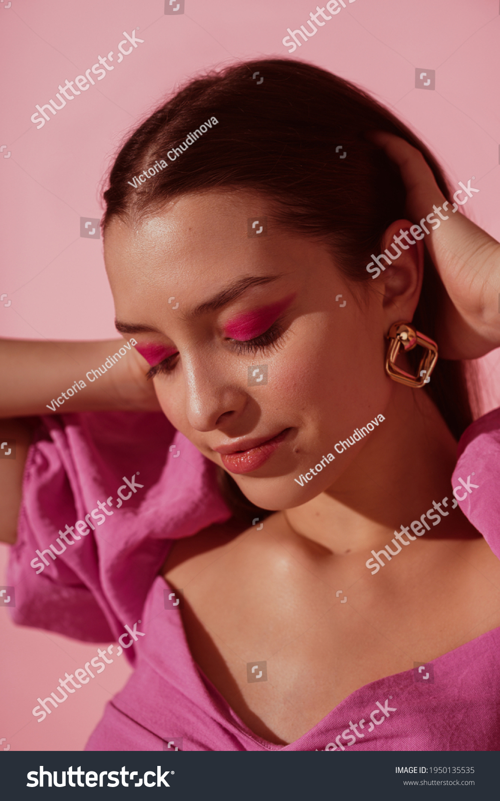 Close up beauty portrait of young beautiful woman with pink, fuchsia color eyeshadow makeup, flawless clean skin, wearing elegant golden earrings, pink blouse. Spring, summer fashion trend #1950135535