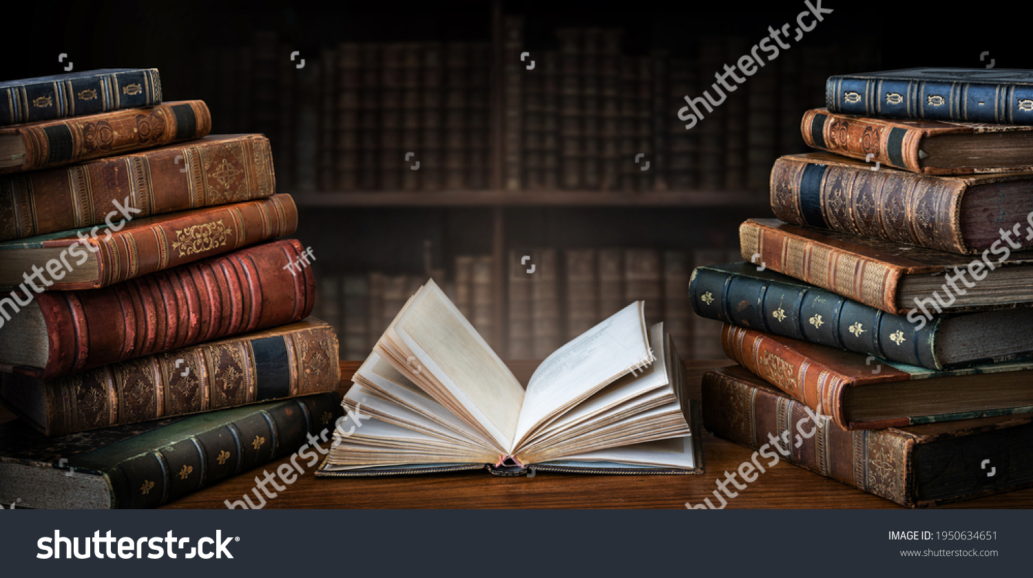 Opened book and stacks of old books on wooden desk in old library. Ancient books historical background. Retro style. Conceptual background on history, education, literature topics. #1950634651