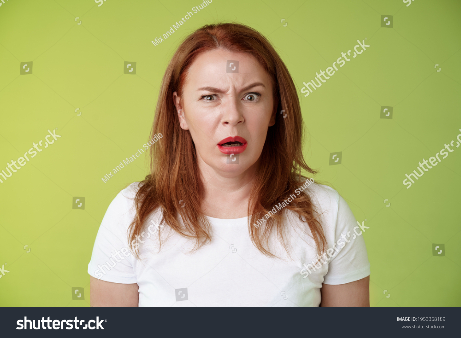 Confused shocked gasping middle-aged redhead woman cringe frustrated puzzled open mouth speechless freak out strange shocking scene stand green background perplexed disappointed #1953358189