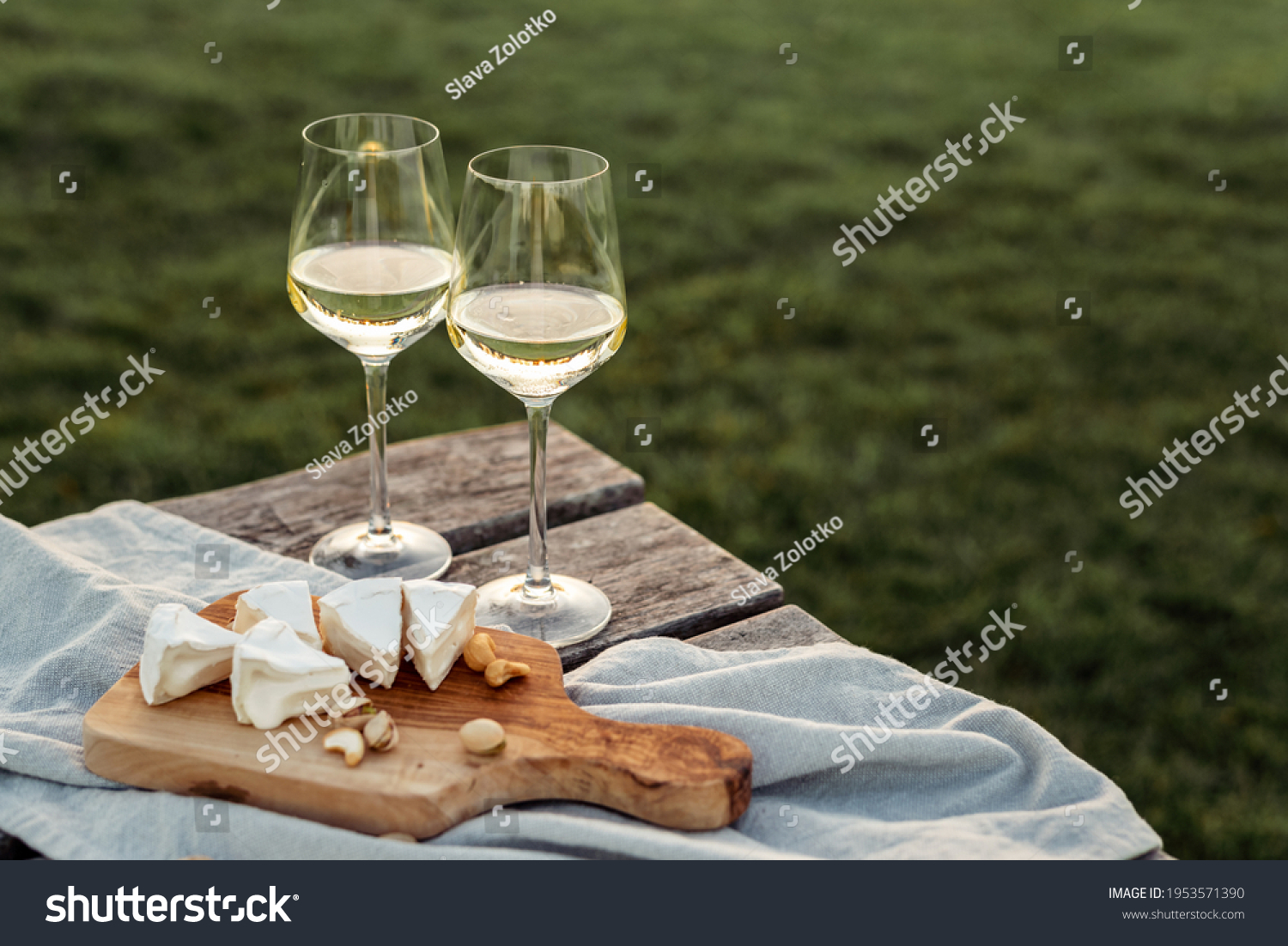 Two glasses of white wine and a wooden plate with cheese and nuts served outside at sunset. #1953571390