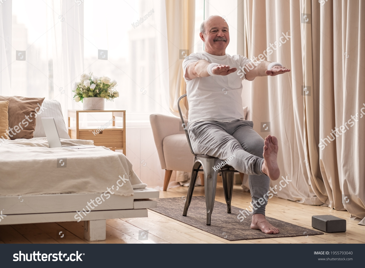 Elderly man practicing yoga asana or sport exercise for legs and hands on chair #1955793040