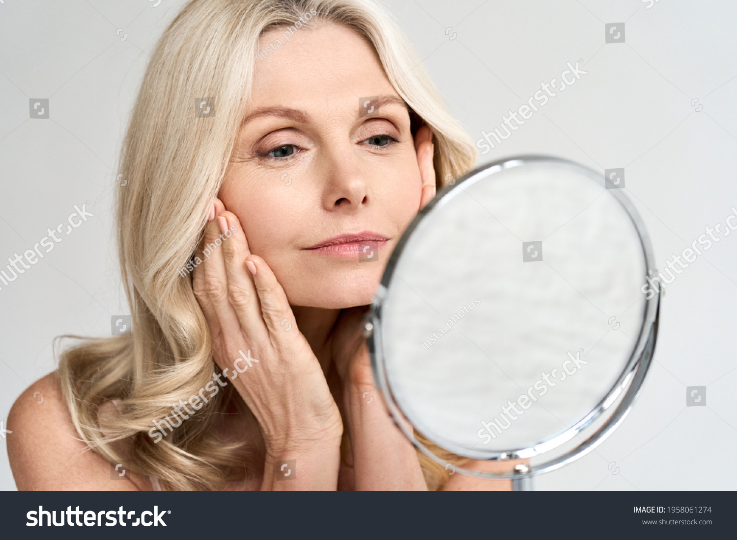 Closeup portrait of gorgeous happy middle age woman looking at mirror touching her skin enjoying treatment for dry skin. Advertising of antiaging beauty skin care products. #1958061274
