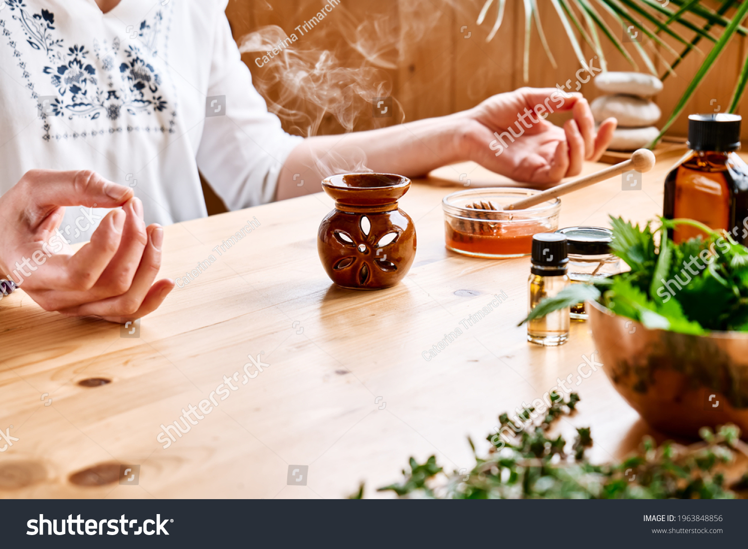 Woman has aromatherapy session at the table with essential oil diffuser medical herbs, different types of oils and essences. Aromatherapy and alternative medicine concept. Natural remedies. #1963848856