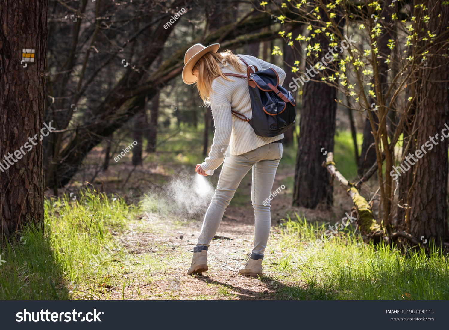 Woman spraying insect repellent against tick at her legs. Protection against mosquito bite during hike in woodland #1964490115