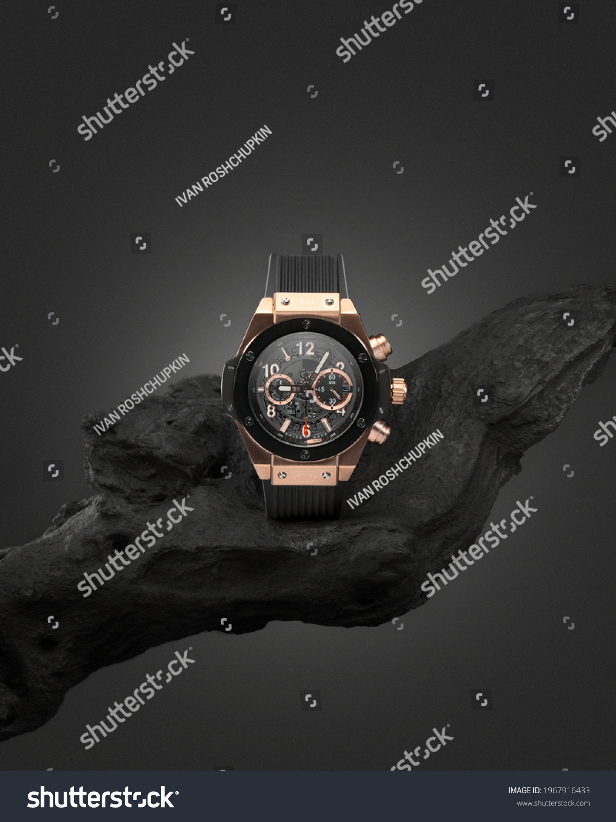 Beautiful gold men's watch with a black strap on a wooden stand, on a gray background. Beautiful gold watch. A luxury brand watch #1967916433