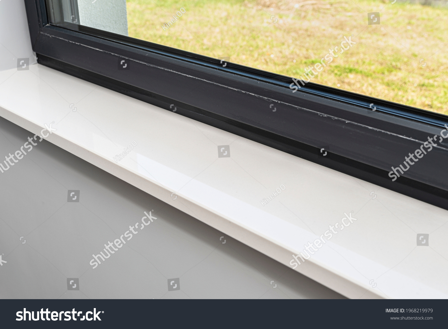 Newly installed white conglomerate window sill inside the room, on the gray walll, visible grass outside the window. #1968219979
