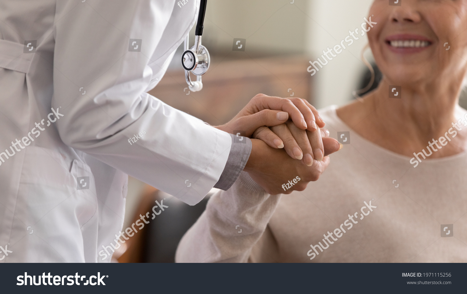 Doctor giving hope. Close up shot of young female physician leaning forward to smiling elderly lady patient holding her hand in palms. Woman caretaker in white coat supporting encouraging old person #1971115256
