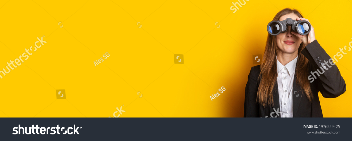 smiling young business woman looking through binoculars on yellow background. #1976559425