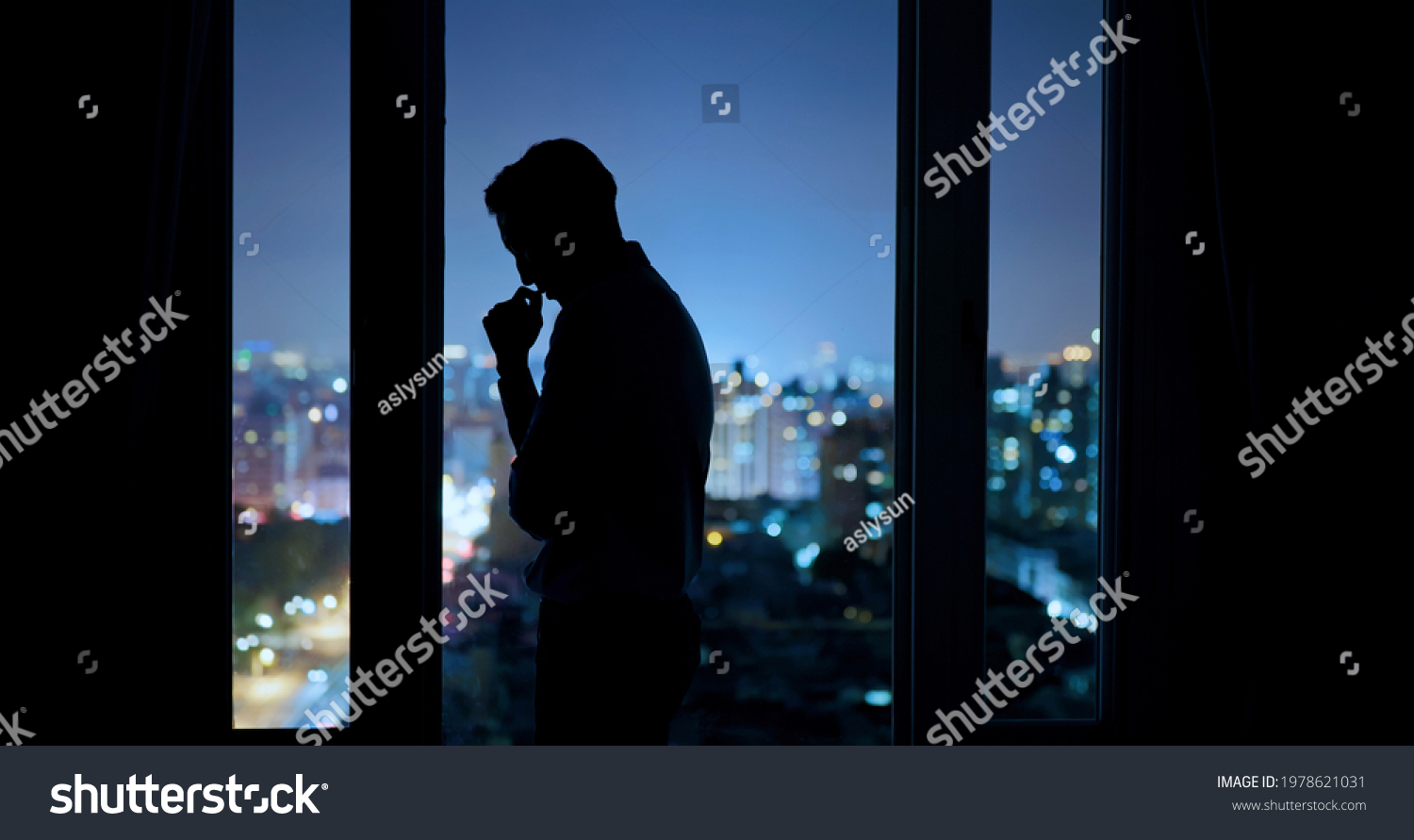 worried asian young businessman is standing near windows while working overtime in office at night #1978621031