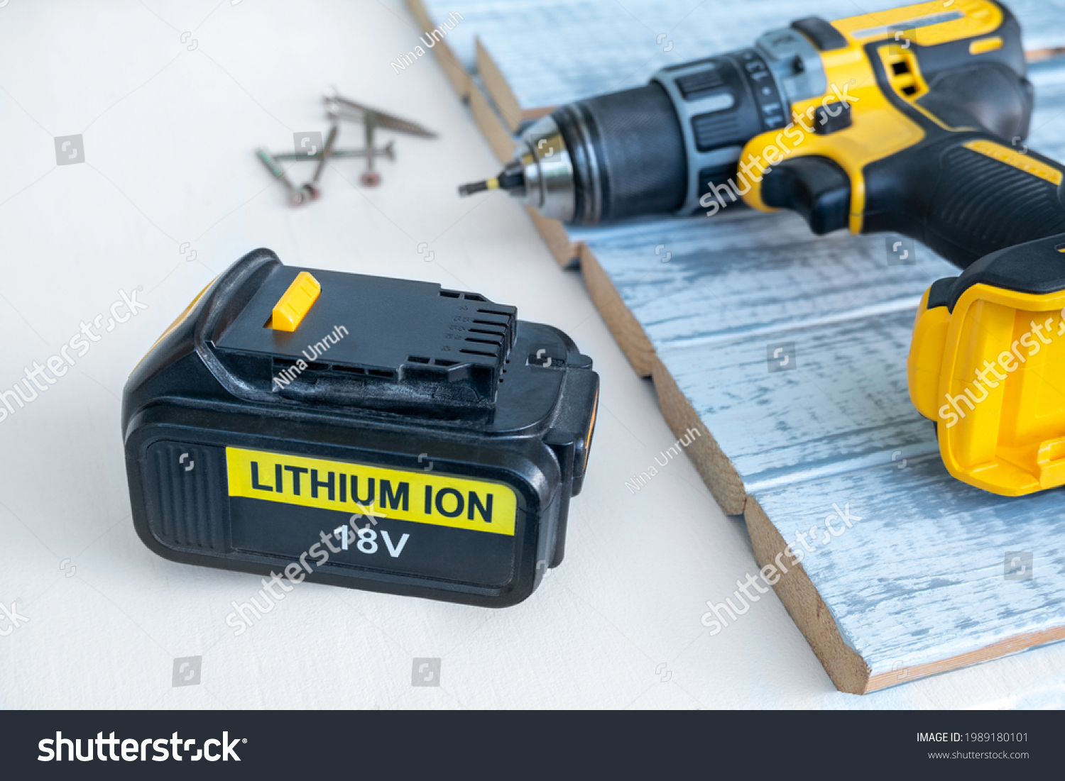 Close up 18 volt recharge Li-ion battery for electric cordless tool,saw,rotary hammer,drill,jigsaw,wrench on white.Blurred screwdriver,screws on gray-painted boards behind.Selective focus, copy space #1989180101