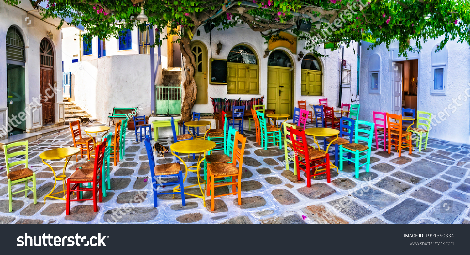 Traditional Greek taverns on the streets. Ios island, old town Chora. Restaurant with colorful typical chairs. Cyclades, Greece #1991350334