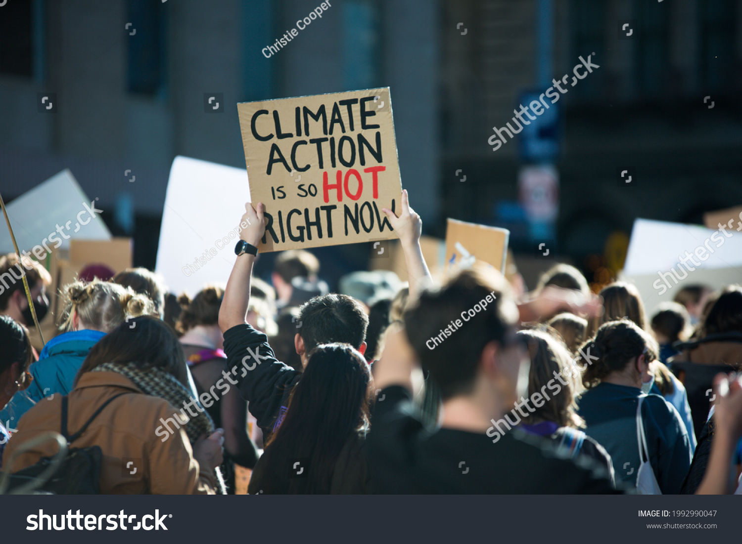 "Climate Action is so hot right now" text written on a sign at student climate change protest in Melbourne Australia. Group of protesters marching down street against global warming. Focus on sign. #1992990047