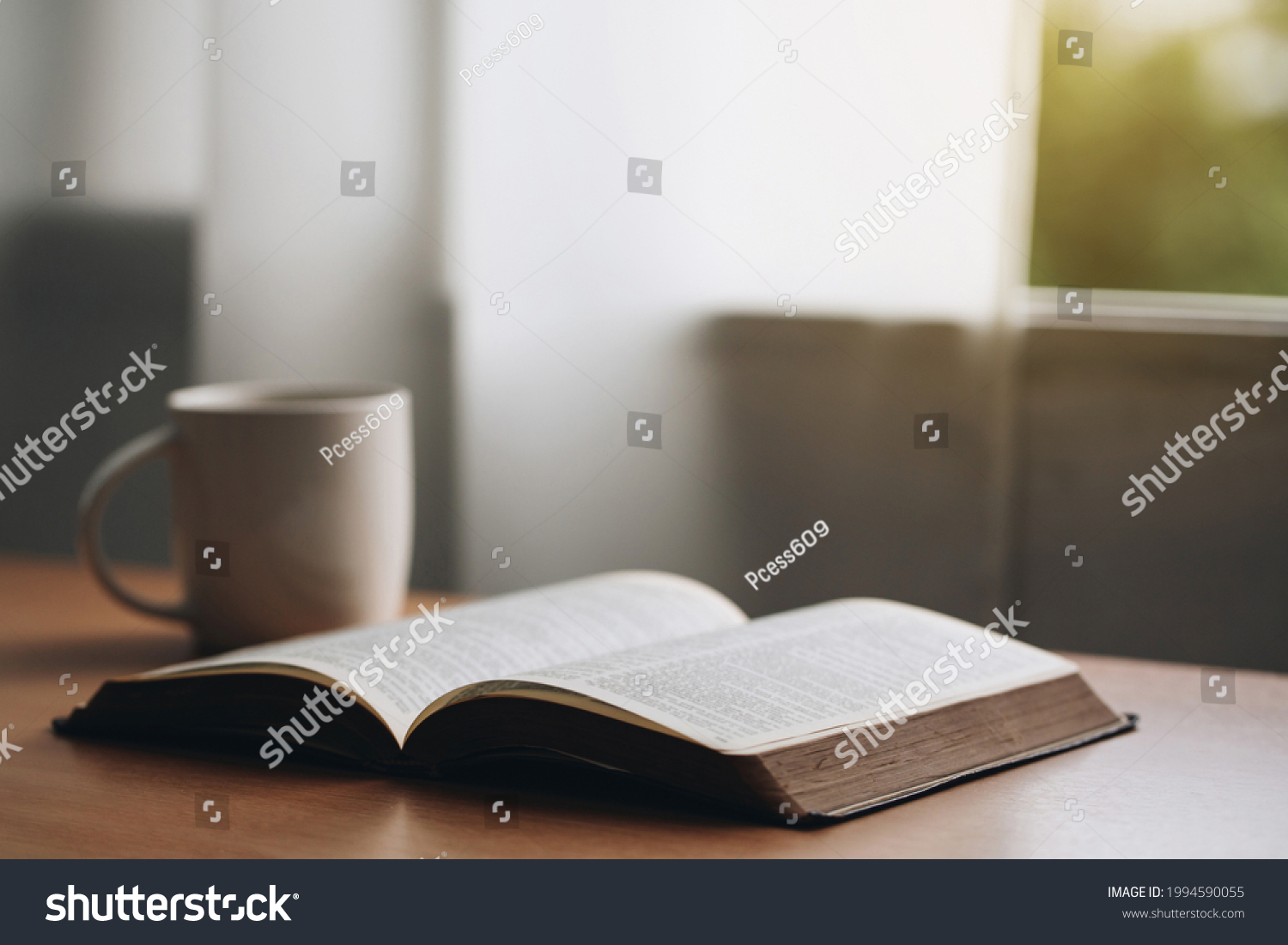 Open bible with a cup of coffee for morning devotion on wooden table with window light.book and coffee cup on wooden table. #1994590055