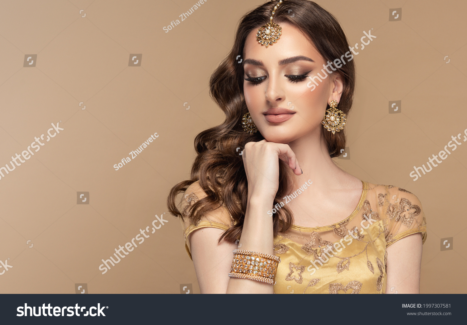 Portrait of beautiful indian girl. Young hindu woman model with golden kundan jewelry set, earrings, tikka and bracelet  . Traditional India costume lehenga choli or saree . Curly hair #1997307581