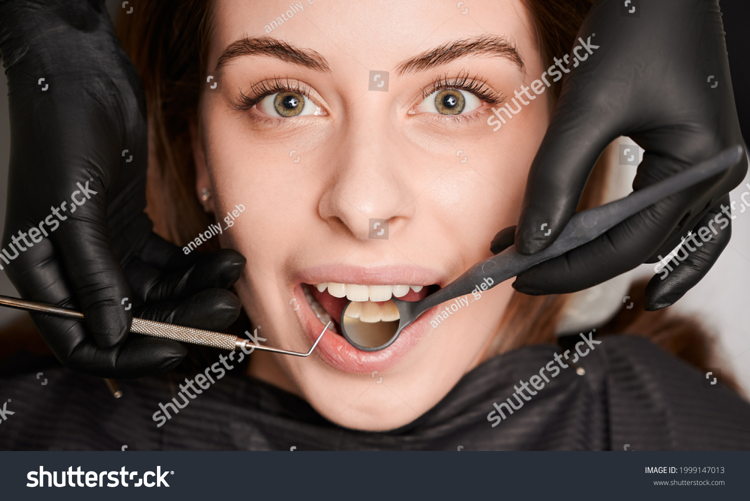 Close up of dentist hands examining woman teeth with dental mirror and explorer. Patient with open mouth while having prophylactic examination in dental clinic. Concept of dentistry and dental care. #1999147013