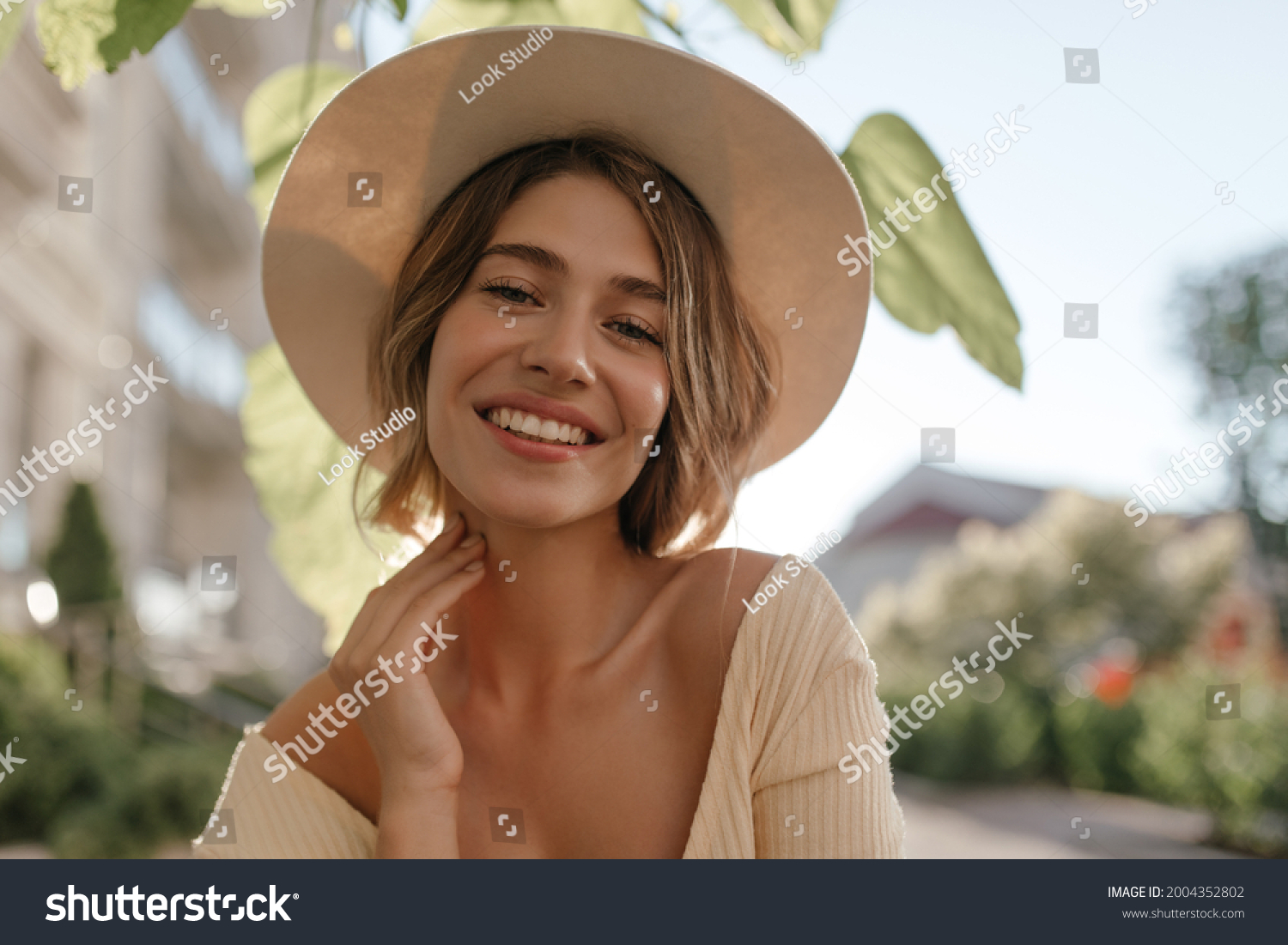 Close-up portrait of lovely white female model with natural make-up expressing good mood. Lovely fair woman in stylish hat holds her chin with her hand. #2004352802