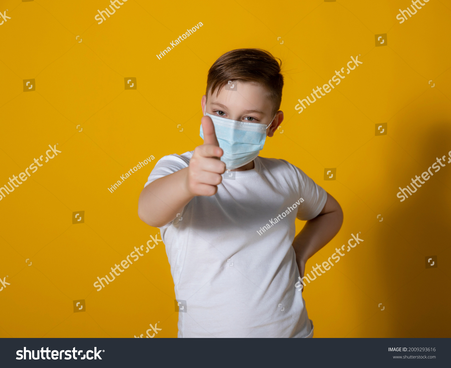 
Teenager boy in a white T-shirt on a yellow background with a medical mask on his face. Points to the mask. Quarantine, virus protection.Photography with different focal lengths. Focus on the face. #2009293616