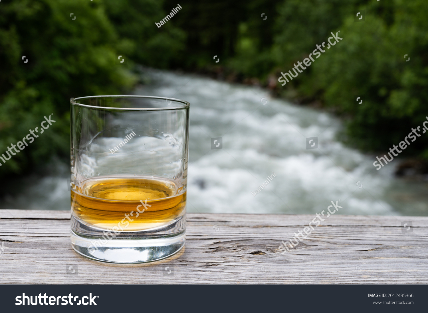 Glass of strong scotch single malt whisky with fast flowing mountain river on background, Scotland #2012495366