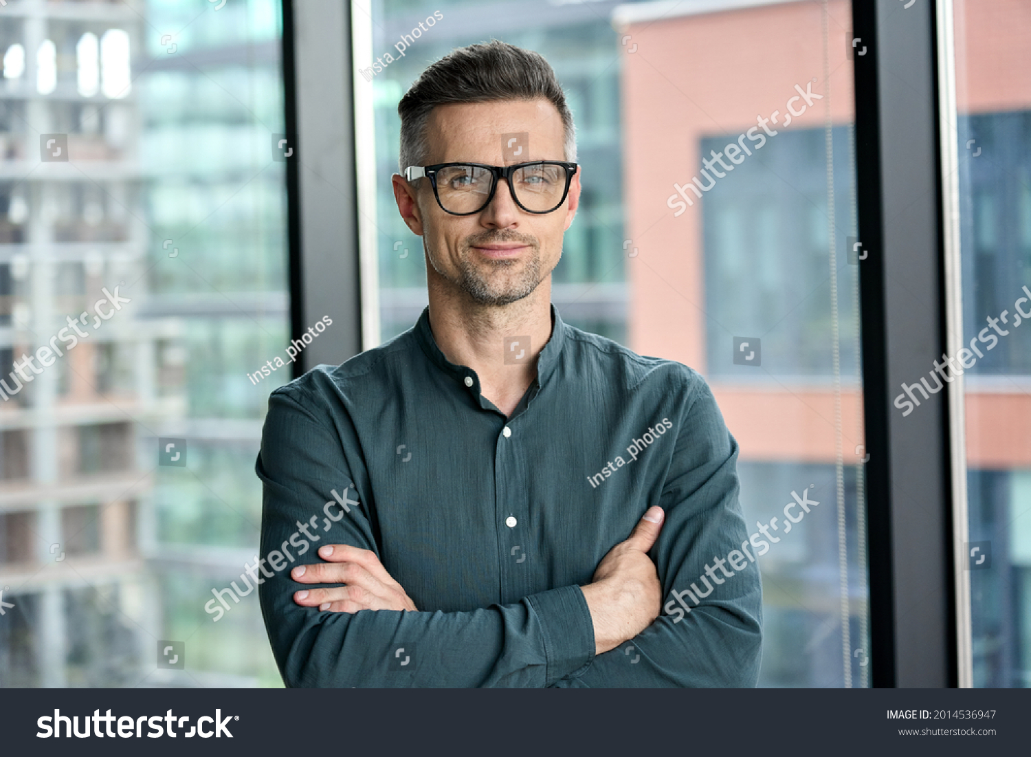 Smiling confident mature businessman looking at camera standing in office. Elegant stylish corporate leader successful ceo executive manager wearing glasses posing for headshot business portrait. #2014536947