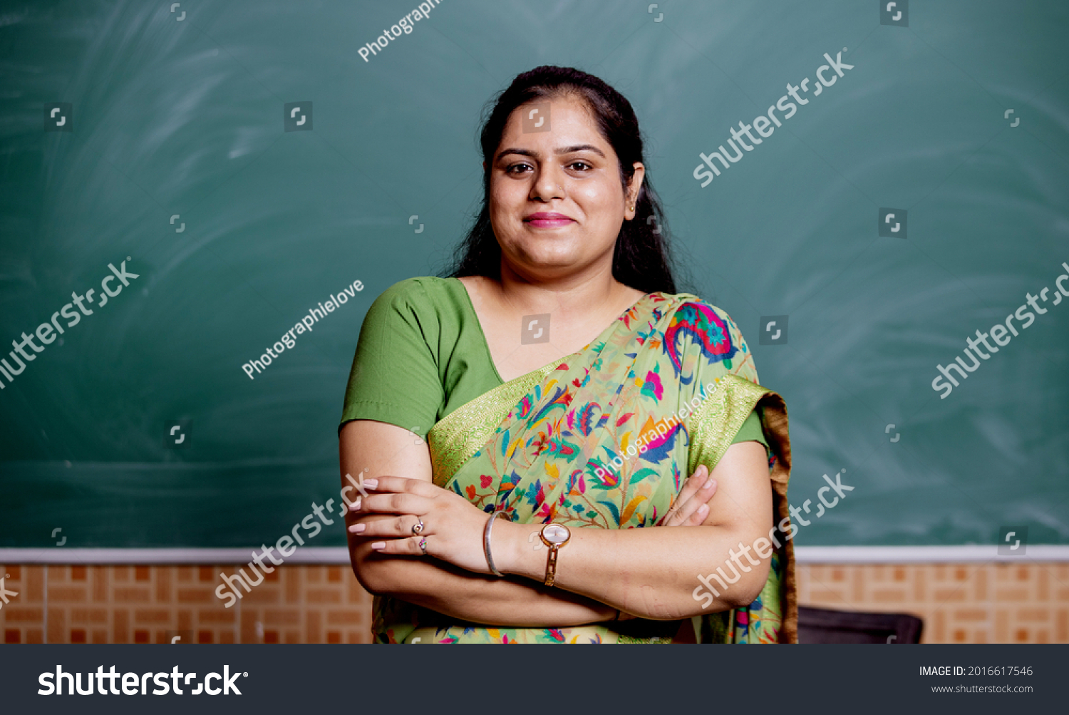 Confident smiling Indian school teacher standing in front of the blackboard in classroom , copy space #2016617546