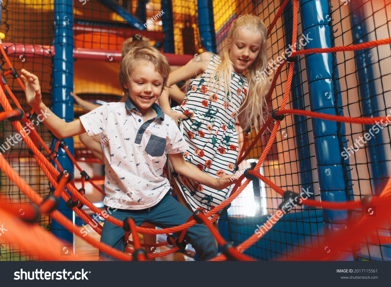 Happy group of siblings playing together on indoor playground. Excited kids playing together on net ropes. Cute school kids playing on the colorful playground at shopping mall #2017115561